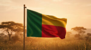 Le drapeau du Bénin, vert, jaune et rouge, flottant dans un paysage africain doré au soleil couchant avec des arbres.